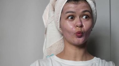 Bir kadın yüzüne nemlendirici bir kozmetik maske takıyor. Yüzünde maske ve kafasında havlu olan bir kadın portresi. Güzellik ve güzellik merkezleri..