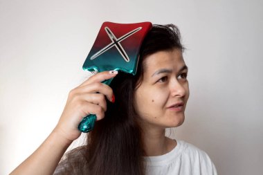 Uzun siyah saçlarını büyük renkli tarağıyla tarayan bir kadın. uzun saçlı günlük rutin