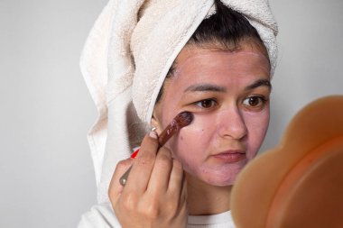 Ev konseptinde yüz bakımı. Yüzüne pembe bir maske takan mutlu genç bir kadın..