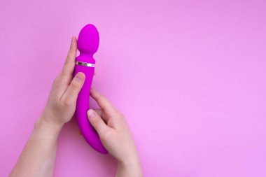 Sex toy pink dildo or vibrator in female hands on a pink background with copy space