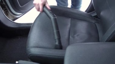 Kirli arabanın içini elektrikli süpürgeyle temizleyen adam.