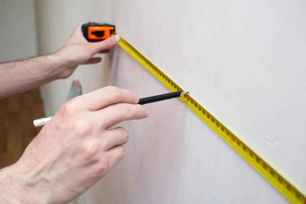 Man reparatie meet de witte wand van de met een meetlint en voor behang. renovatie appartement — Stockfoto