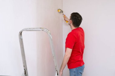 Duvarı silindirle kaplayan bir adam. İçerisinin tamiri. Genç erkek dekoratör boş odada bir duvar boyuyor. Yenileme işini kendin yap.