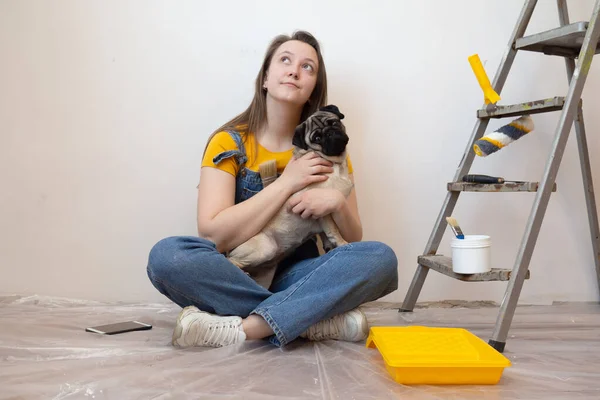 Mujer joven independiente con perro pug planificación renovación apartamento sentado en el piso con herramienta de construcción. bricolaje reparación propietario manos con mascota. — Foto de Stock