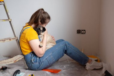 Bekar bir kadın yenileme, inşaat aletleri ve arka planda merdiven varken evcil köpeğiyle yerde oturuyor ve dinleniyor. Evcil hayvanlı bağımsız bekar kadın hayatı.