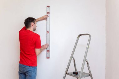 Kabarcık seviyesindeki aletle duvarın seviyesini kontrol eden tamirci. Yenileme konsepti. 