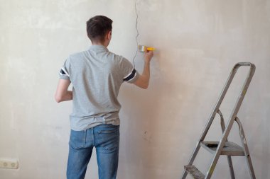 İnşaat işçisi bir evin çatlak duvarını onarıyor, duvara çimento yapıştırıyor. İnşaatçı, macun bıçağıyla duvardaki bir çatlağa beyaz çimento sürüyor. 