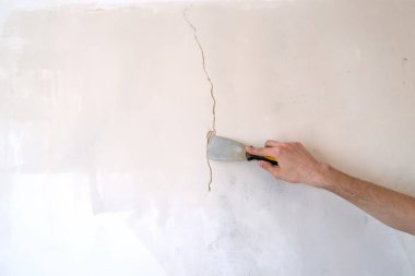 İnşaat işçisi bir evin çatlak duvarını onarıyor, duvara çimento yapıştırıyor. Müteahhit, macun bıçağıyla duvardaki bir çatlağa beyaz çimento sürüyor. Kapat. 