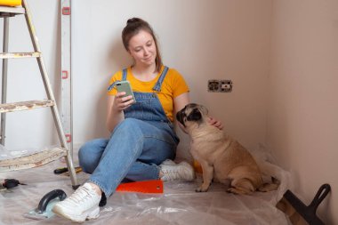 Bekar bir kadın yenileme, inşaat aletleri ve arka planda merdiven varken evcil köpeğiyle yerde oturuyor ve dinleniyor. Evcil hayvanlı bağımsız bekar kadın hayatı 