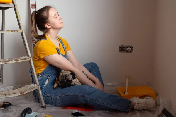 Independent single female sitting on floor and rest with pet dog in her new house during renovation, construction tools and ladder on the background. Independent single female life with pet