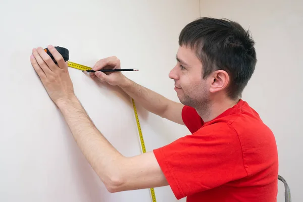 Homme réparation mesure le mur blanc de la avec un ruban à mesurer et avant tapisserie. appartement de rénovation — Photo