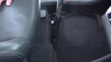 Kirli arabanın içini elektrikli süpürgeyle temizleyen adam.