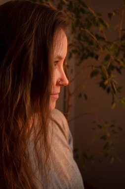 Gün batımının sıcacık ışınlarında genç bir kadın. İçerideki kızın sıcak sakin portresi. Yüzünde ışık ve gölge.