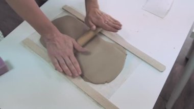 Kadın seramik atölyesinde ahşap merdane kullanarak kil yuvarlıyor. Eller yakın çekim. Çömlek oluşturuluyor.
