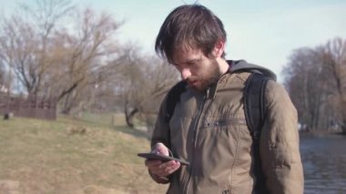 Açık havada akıllı telefon kullanan sıradan bir adam. Yakışıklı, sakallı, Avrupalı, parkta mesajlaşan yaratıcı erkek.