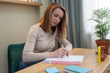 Kadın masada oturuyor ve kişisel günlüğündeki kalemle bir not yazıyor. iş planlaması ve kağıt biçiminde kayıt tutma