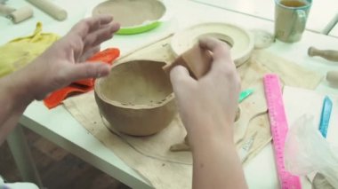 Çömlekçi kadın çömlek atölyesinde kilden kupa yapıyor. Seramik bardak oluşturma süreci. El yapımı, hobi sanatı ve el işi konsepti.