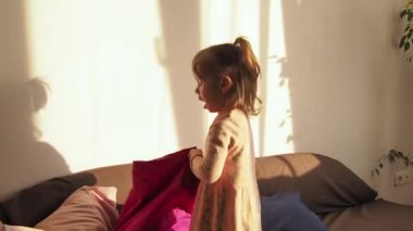 Küçük kız kanepede zıplayarak eğleniyor. Mutlu ve neşeli bir çocuk, evcimen olmalı.