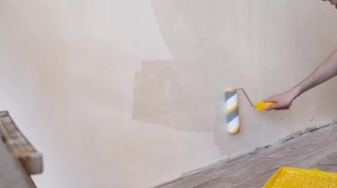 Duvarı silindirle kaplayan bir adam. İçerisinin tamiri. Genç erkek dekoratör boş odada bir duvar boyuyor. Yenileme işini kendin yap.