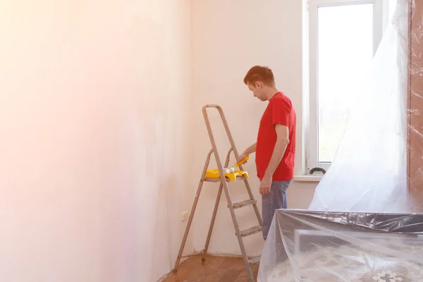 Man priming the wall with a roller. Repair of the interior. Young male decorator painting a wall in house. Concept renovation do it yourself. — Stock Photo, Image
