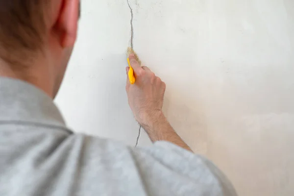 Bouwvakker repareert een barsten muur van een huis, pleisterwerk cement op de muur. Bouwer aanbrengen van wit cement op een scheur in een muur met een stopmes. — Stockfoto