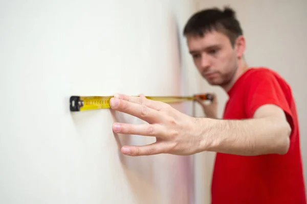 Homme réparation mesure le mur blanc de la avec un ruban à mesurer et avant tapisserie. appartement de rénovation — Photo
