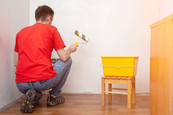 Man priming the wall with a roller. Repair of the interior. Young male decorator painting a wall apartment. Concept renovation do it yourself. — Stock Photo, Image