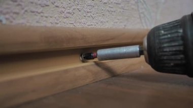 Elinde tornavida olan bir işçi dairedeki süpürgeliğin vidalarını söküyor. Kapat.