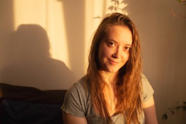 Gün batımının sıcacık ışıklarıyla kameraya bakan genç bir kadın. İçerideki kızın sıcak sakin portresi. Yüzünde ışık ve gölge