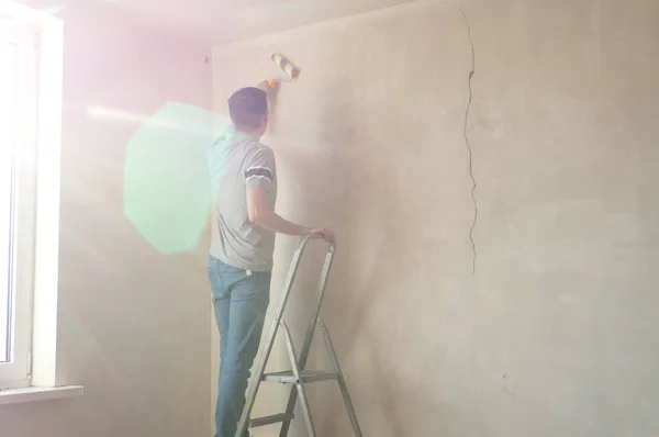 Een man die de muur met een roller klaarmaakt. Reparatie van het interieur. Jonge mannelijke decorateur schildert een muur in de lege kamer. Concept renovatie doe het zelf. — Stockfoto