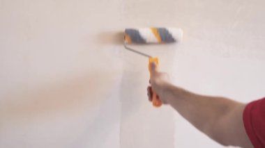 Duvarı silindirle kaplayan bir adam. İçerisinin tamiri. Genç erkek dekoratör boş odada bir duvar boyuyor. Yenileme işini kendin yap..