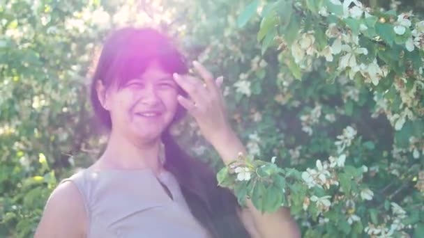 Retrato de mujer sonriendo en rama floreciente de un árbol con enfoque selectivo. Joven hermosa mujer disfruta del aroma de las flores en el jardín. — Vídeo de stock