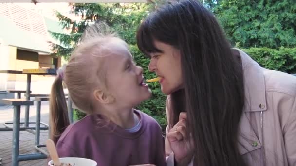 Madre e hija compartiendo papas fritas y comiendo divertidas juntas. Chicas se divierten en la terraza. — Vídeos de Stock