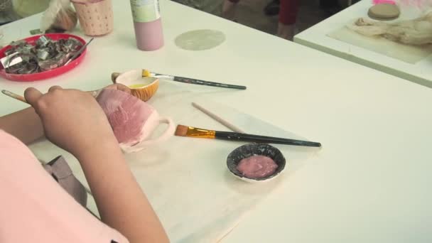 Girl painting with brush on clay pottery cup in ceramic workshop studio. Development of art and painting in children. Close-up. — Stock Video