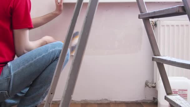 Een man die de muur met een roller klaarmaakt. Reparatie van het interieur. Jonge mannelijke decorateur schildert een muur in de lege kamer. Concept renovatie doe het zelf. — Stockvideo