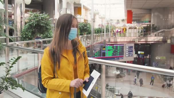 Jonge moderne toeristische vrouw in het geel met gezicht medisch masker op de luchthaven of het station. Reizen tijdens de coronavirus pandemie en toerisme na het einde van quarantaine covid 19. nieuwe normale. — Stockvideo