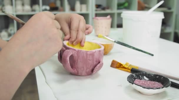 Girl painting with brush on clay pottery cup in ceramic workshop studio. Development of art and painting in children. Close-up. — Stock Video