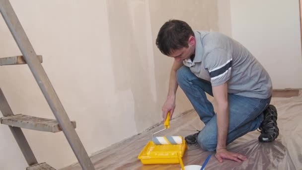 Duvarı silindirle kaplayan bir adam. İçerisinin tamiri. Genç erkek dekoratör boş odada bir duvar boyuyor. Yenileme işini kendin yap.. — Stok video