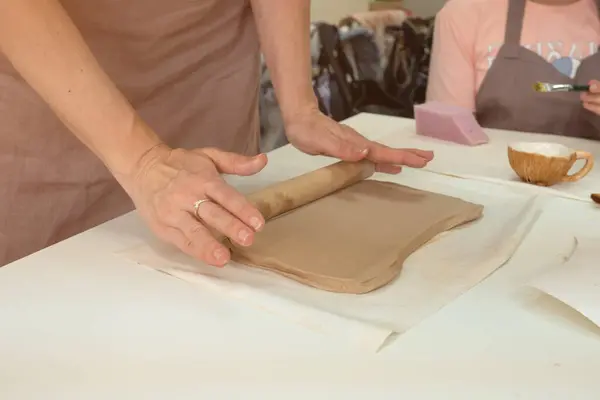 La ceramista femenina rueda la arcilla usando un rodillo de madera en un estudio de cerámica. De cerca las manos. Creación de cerámica —  Fotos de Stock