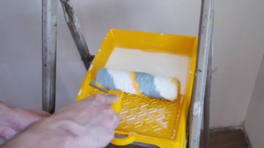 Dekoratör, astarı sarı tepsiden silindirle alıyor. Yenileme odasında onarım.