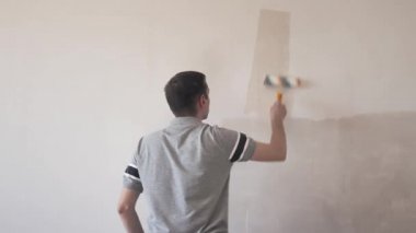 Duvarı silindirle kaplayan bir adam. İçerisinin tamiri. Genç erkek dekoratör boş odada bir duvar boyuyor. Yenileme işini kendin yap..