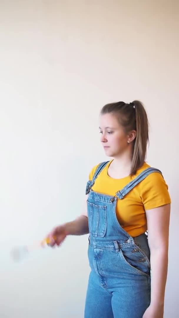 Mujer feliz con cepillo mira a la cámara una pared sin pintar en el fondo. Independiente hembra sola hace reparaciones de bricolaje en su apartamento — Vídeo de stock