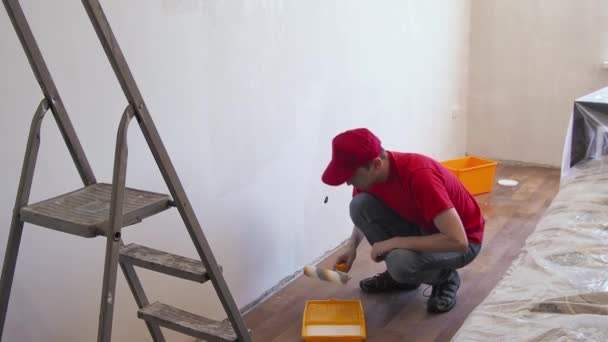 Een man die de muur met een roller klaarmaakt. Reparatie van het interieur. Jonge mannelijke decorateur schildert een muur in de lege kamer. Concept renovatie doe het zelf. — Stockvideo