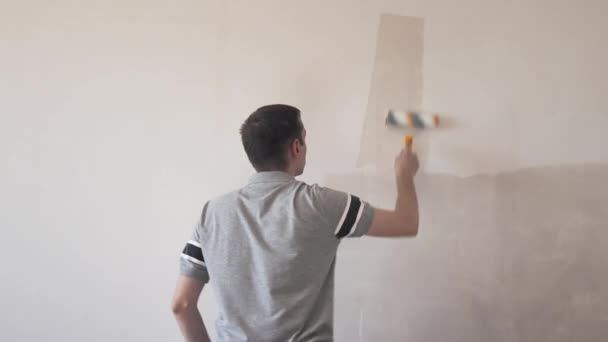 Un uomo che attacca il muro con un rullo. Riparazione degli interni. Giovane decoratore di sesso maschile che dipinge un muro nella stanza vuota. Concetto rinnovamento fai da te. — Video Stock