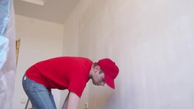 Duvarı silindirle kaplayan bir adam. İçerisinin tamiri. Genç erkek dekoratör boş odada bir duvar boyuyor. Yenileme işini kendin yap..
