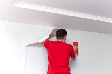 Duvara duvar kağıdı yapıştıran genç profesyonel bir tamirci. Apartman onarımı. Ev yenileme konsepti.