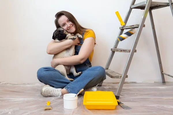 Mujer abraza perro mascota en su nueva casa durante la renovación, herramientas de construcción y escalera en el fondo. Vida femenina individual independiente con mascota. — Foto de Stock