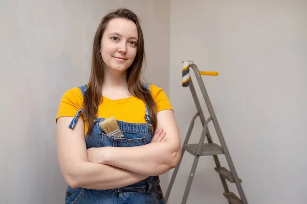 Joven reparadora profesional con un pincel para pintar en escalera de fondo y pared de cemento gris. Independiente hembra sola hace reparaciones en su apartamento. — Foto de Stock