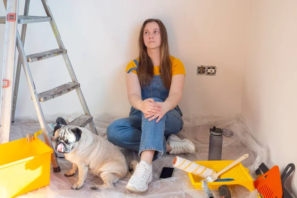Mujer joven independiente con perro pug planificación renovación apartamento sentado en el piso con herramienta de construcción. bricolaje reparación propietario manos con mascota. — Foto de Stock