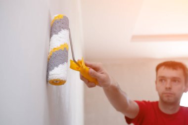 Duvarı seçici odaklı silindirle kaplayan adam. İçerisinin tamiri. Genç erkek dekoratör odada bir duvar boyuyor. Yenileme işini kendin yap..